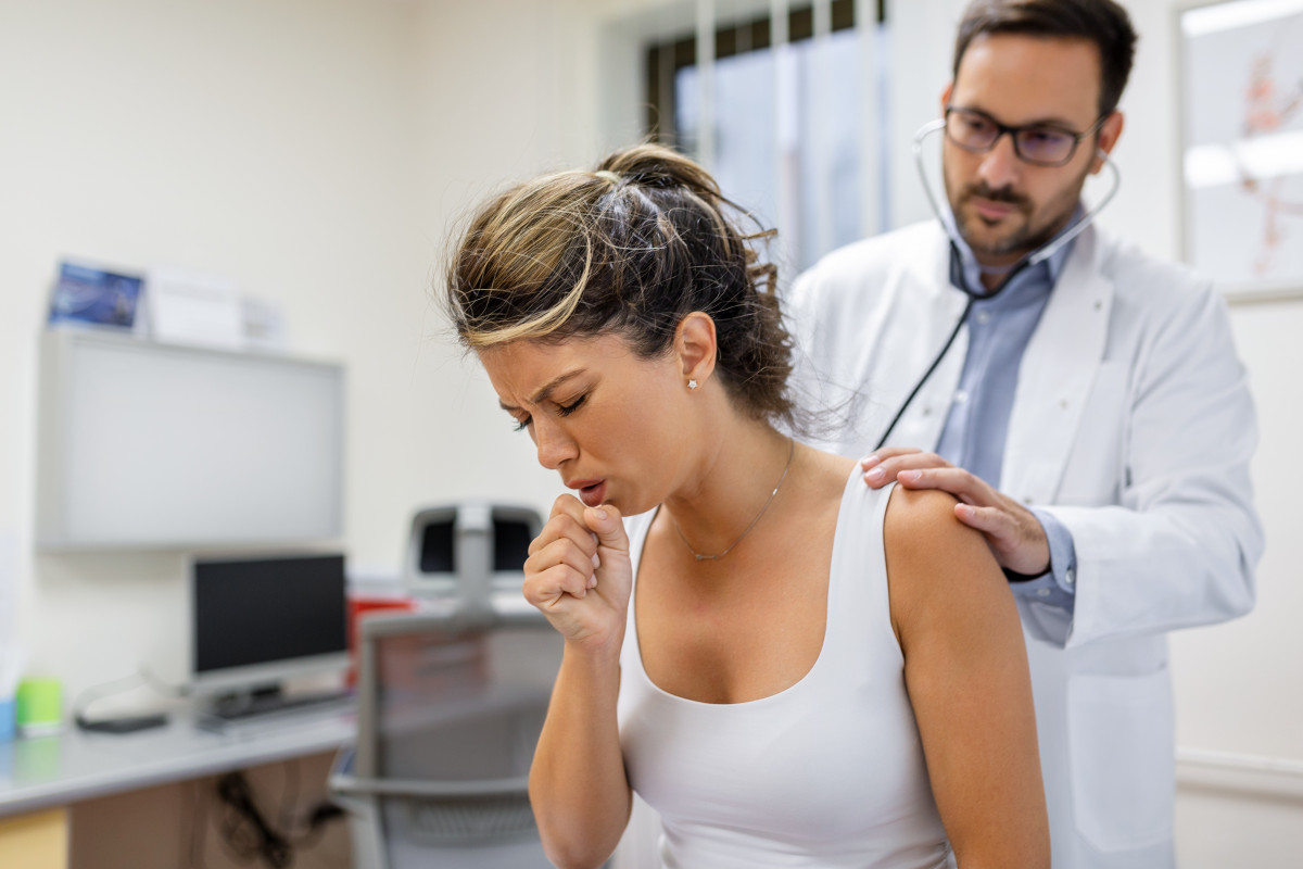 Young female patient clinic suffered from pneumonia she is coughing doctor listens wheezing lungs with stethoscope