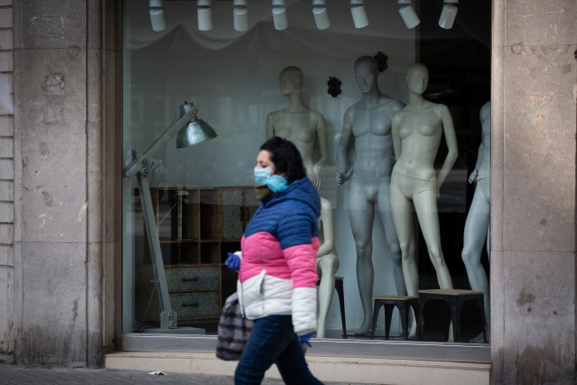 Una mujer protegida con una mascarilla pasa junto a un escaparate de una tienda cerrada durante el noveno día laborable desde que se decretó el estado de alarma en el país a consecuencia del coronavirus, en Barcelona/Catalunya (España) a 26 de marzo de 20