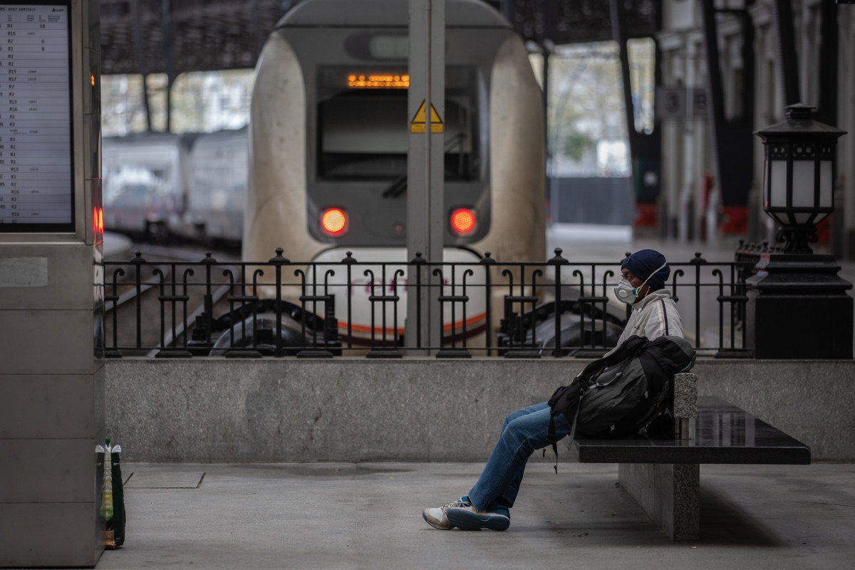 Un home protegit amb una màscara espera assegut en un banc en una estació de tren de Barcelona durant el segon dia laborable de l'estat d'alarma pel coronavirus, a Barcelona (Espanya), a 17 de març de 2020.