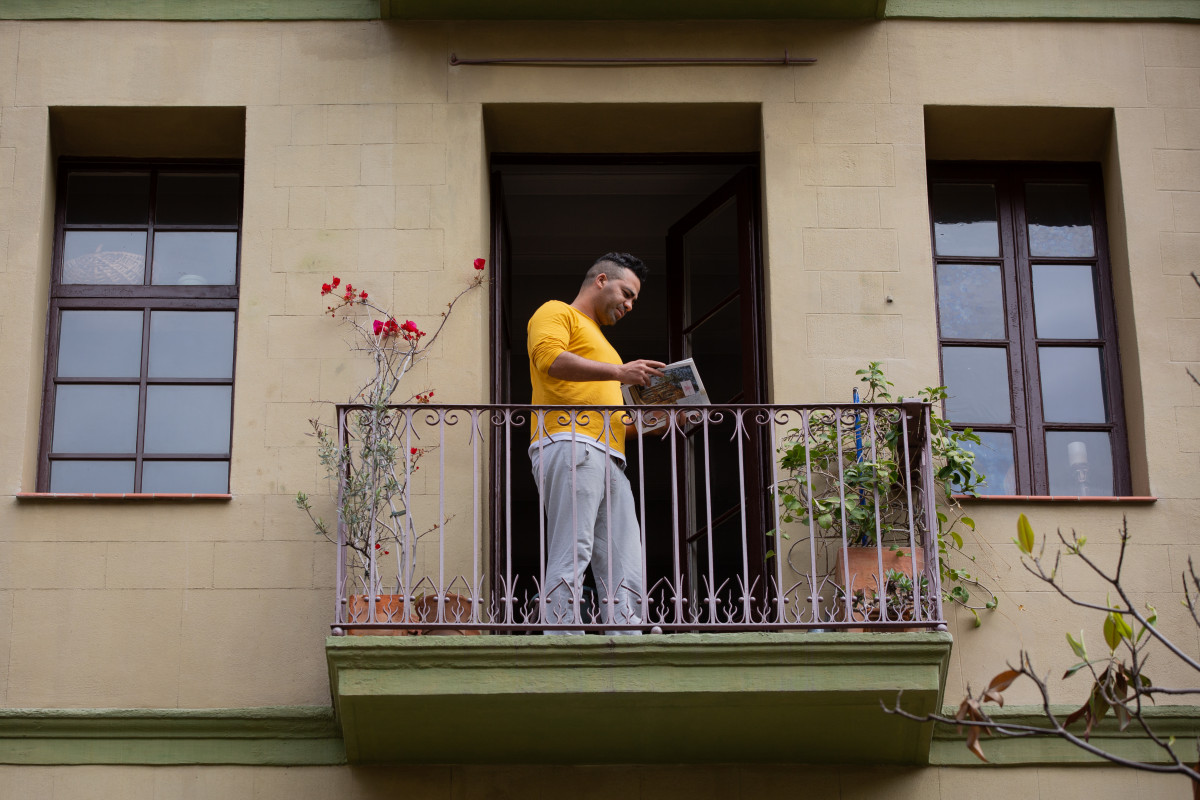 Un home llegeix 1 llibre a l'balcó de casa su durante la Diada de Sant Jordi de l'any 2020.
