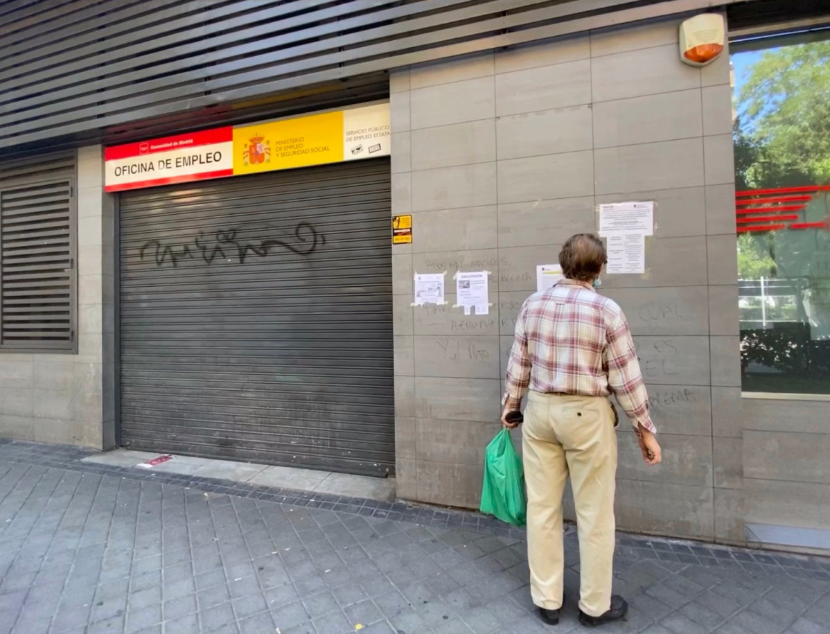Una persona observa un dels cartells amb instruccions per fer tràmits per internet col·locats a la façana d'una oficina de l'SEPE