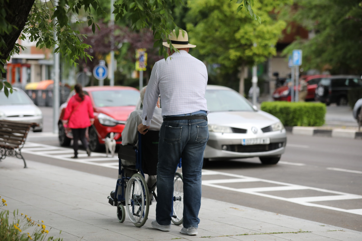 Un home passeja a una persona d'edat avançada en cadira de rodes durant la seva franja horària permesa a la desescalada per la crisi de l'Covid-19 on aquells majors de 70 anys poden sortir a la via pública de 10.00 a 12.00 hores i de 19.00 a 20.00 ho