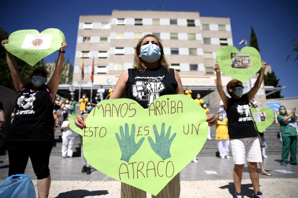Una treballadora de neteja de l'Hospital Gregorio Marañón subjecta un cor verd-que reivindica la importància dels serveis públics en Sanitat- en què resa 'Mans dalt això és un atracament' a les portes de l'hospital.