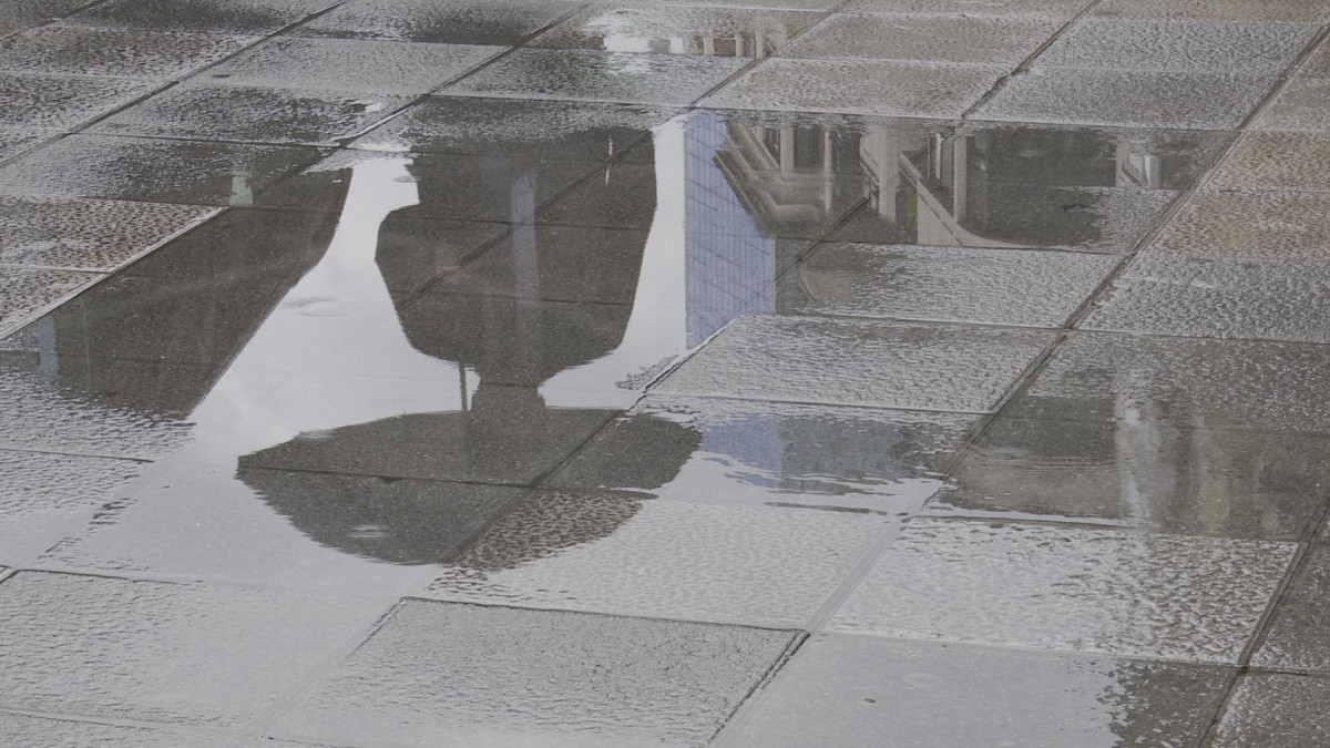 Una persona amb paraigües es reflecteix en un toll provocat per la pluja aquest matí a Bilbao.