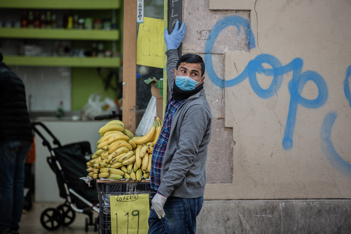 Un home protegit amb mascareta i guants a la porta del seu establiment d'alimentació al barri de Raval (Arxiu)