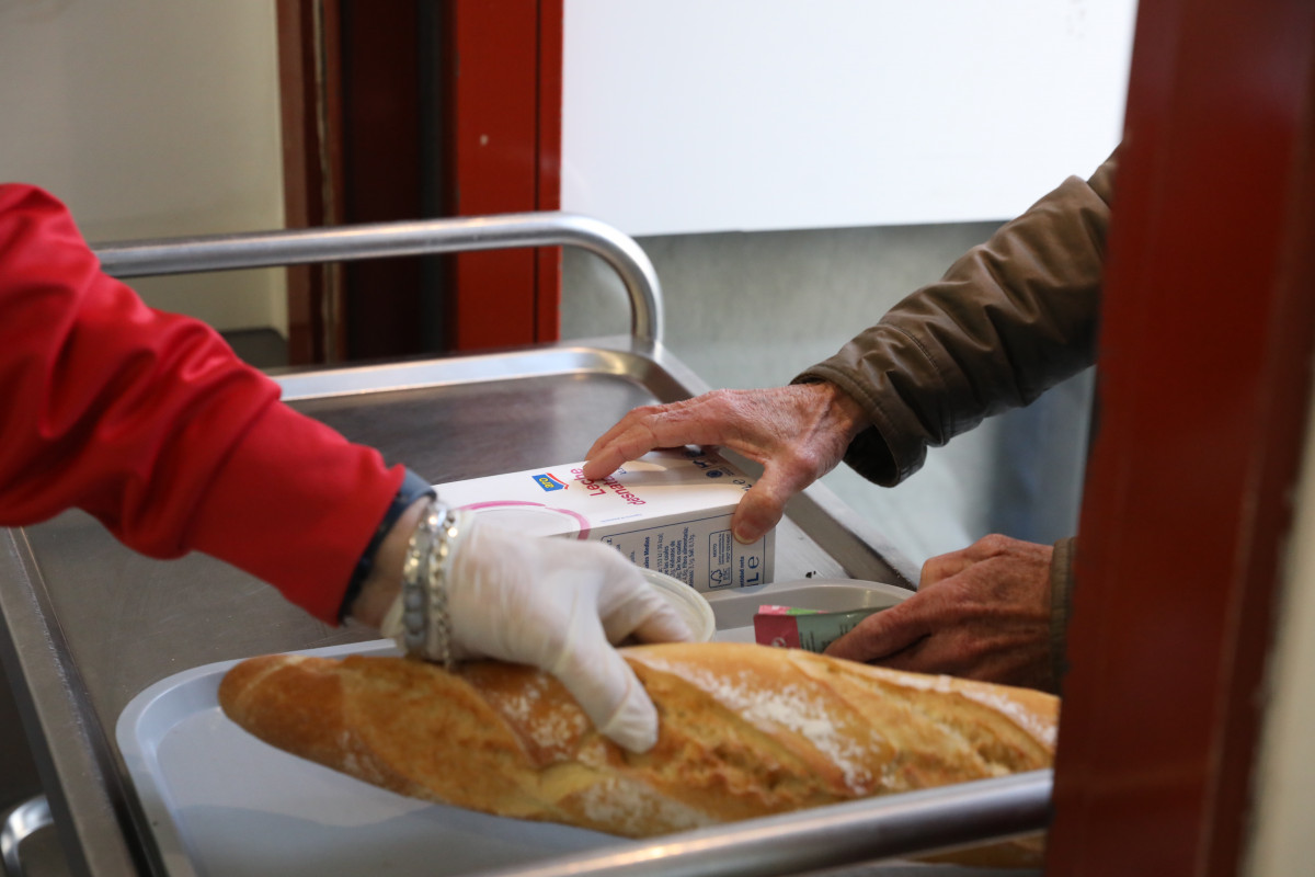 Un voluntari (i) porta menjar a una persona (d) com a part de l'repartiment diari d'aliments de l'Menjador Social Sant Josep, a Puente de Vallecas, Madrid (Espanya), a 5 de febrer de 2021.