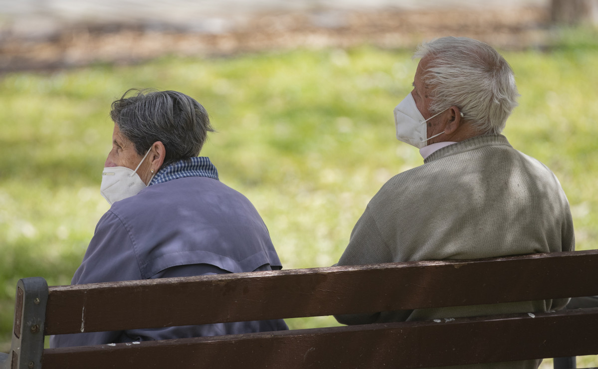 Un home i una dona gran, asseguts en un banc i amb mascareta, al Parc de l'Manzanares, el dia en què entra en vigor l'ús obligatori de màscara fins i tot amb distància de seguretat, a Madrid (Espanya), a 31 de març de 2021.