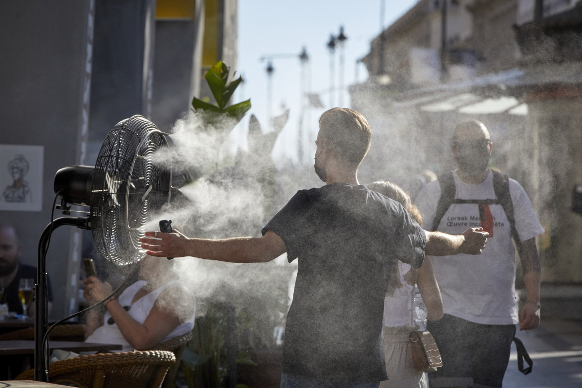 Un noi es refresca de la calor amb un difusor de vapor d'aigua d'un restaurant del carrer Alcalá, a Madrid