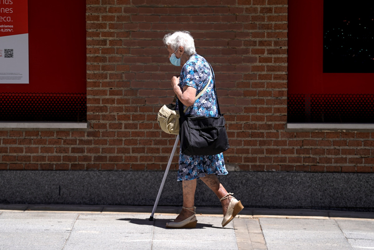 Una dona gran amb mascareta camina pel carrer ajudada d'una crossa, a 27 de juliol de 2021, a Madrid, (Espanya).