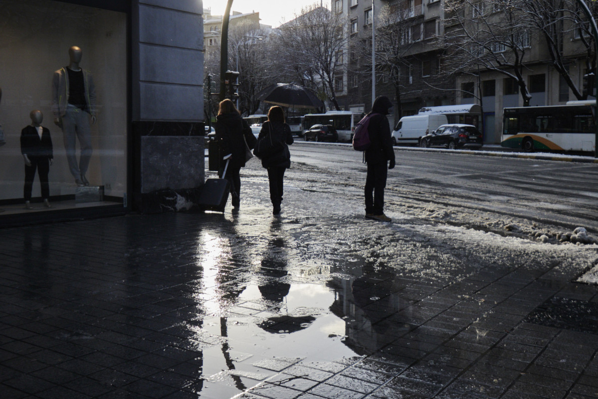 Varias personas camina por una acera con charcos de nieve derretida, a 2 de abril de 2022, en Pamplona, Navarra (España).