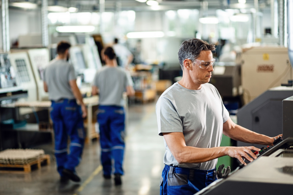 Treballador adult mitjà que opera màquina cnc mentre treballa instal·lació industrial
